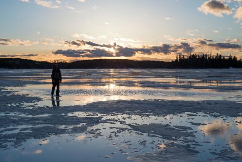 Bearded outdoorsman on melting lake ice, sunset behind him.