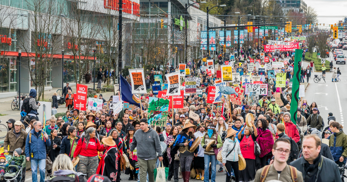 A group of people marching down the street, protesting Kinder Morgan and the Trans Mountain pipeline. End of image description.