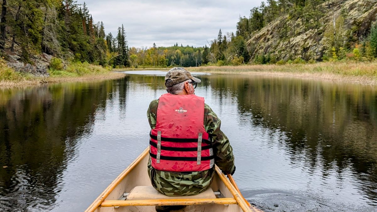 A man in a canoe on a river surrounded by forests. end of image description.