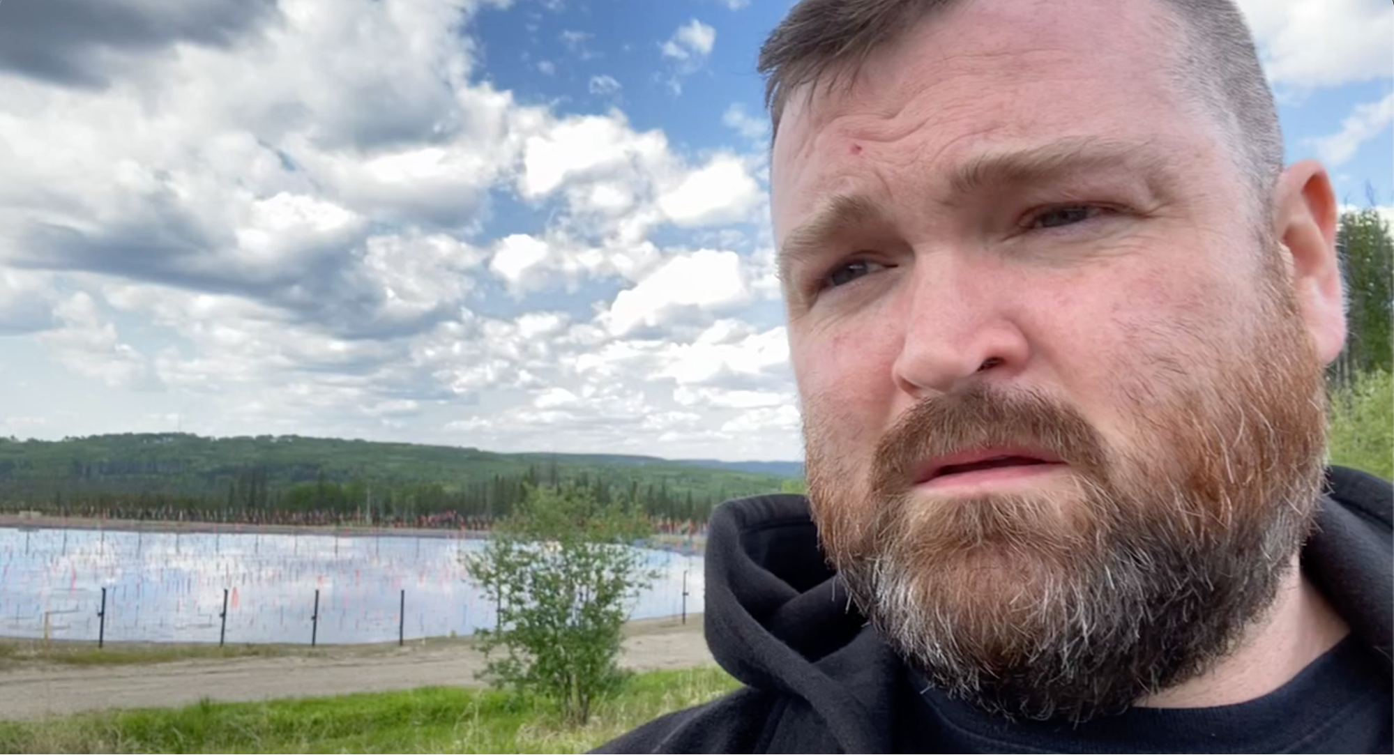 A man looking unimpressed next to a fracking wastewater containment tank. End of image description.