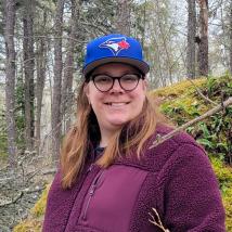 A female presenting person wearing a baseball cap and smiling at the camera. End of image description.