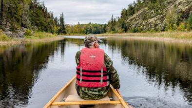 A man in a canoe on a river surrounded by forests. end of image description.