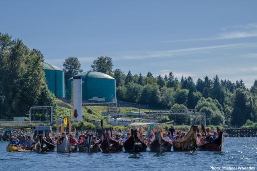 A flotilla of canoes and Kayaks floats in Burrard inlet in front of the Kinder Morgan oil tank facility