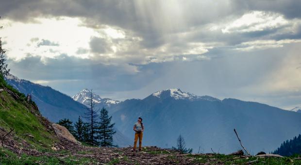 A bright and cloudy sky above a mountainous landscape where a woman stands looking up.